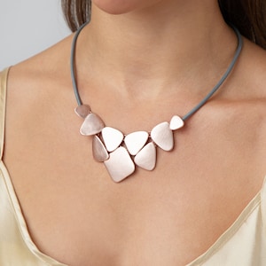 May include: A rose gold necklace with a geometric design. The necklace is made of multiple pieces of metal that are connected together to form a unique and modern look. The necklace is worn by a person with a light skin tone.