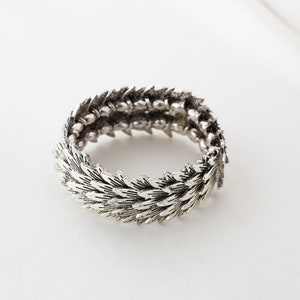 Könnte beinhalten: Silberfarbener Armreif mit einem Blattdesign. Der Armreif ist aus Metall und hat ein flexibles Design.