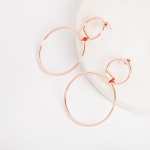 May include: Rose gold double hoop earrings with a smaller hoop inside the larger hoop.