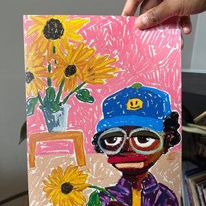 Puede incluir: Un dibujo colorido de una persona que lleva un sombrero azul con una cara sonriente amarilla, gafas y una camisa morada, sosteniendo un girasol amarillo. El fondo es rosa con tres girasoles amarillos en un jarr&oacute;n sobre una mesa de madera.