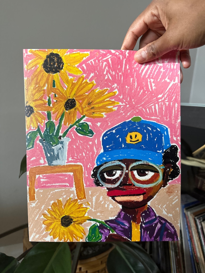 Puede incluir: Un dibujo colorido de una persona que lleva un sombrero azul con una cara sonriente amarilla, gafas y una camisa morada, sosteniendo un girasol amarillo. El fondo es rosa con tres girasoles amarillos en un jarr&oacute;n sobre una mesa de madera.