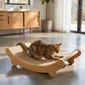 K&ouml;nnte beinhalten: Eine hellbraune getigerte Katze liegt auf einem Kratzbaum aus Holz. Der Kratzbaum hat ein geschwungenes, schaukelndes Design mit einer gewebten Sisal-Kratzfl&auml;che. Der Rahmen besteht aus hellem Holz.