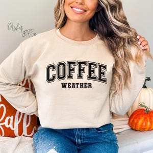 May include: A beige sweatshirt with the text "COFFEE WEATHER" in black block letters.