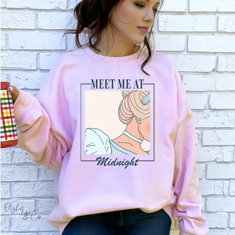 May include: Pink sweatshirt featuring a graphic of Cinderella's silhouette and the text "Meet me at Midnight".