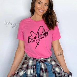 May include: Pink t-shirt with a black graphic that says "Be a buddy not a bully" with a heart and an X.