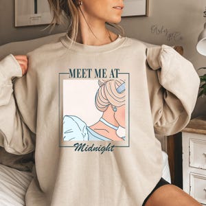 May include: A beige sweatshirt with a graphic print of a cartoon Cinderella with the text "Meet me at Midnight".
