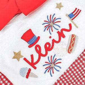 May include: White t-shirt with red, white, and blue embroidered Fourth of July themed designs. The designs include a top hat, fireworks, a hot dog, ice cream cone, and the word "keen".
