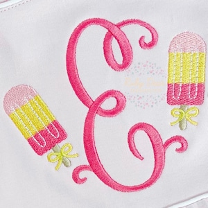 May include: Pink embroidered letter E with two pink, yellow, and white popsicle designs on a pink fabric background.