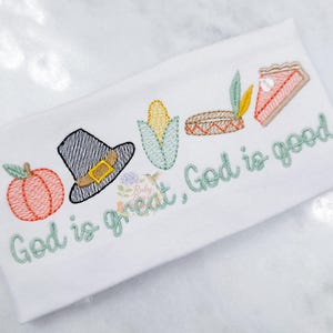 May include: White fabric embroidered with Thanksgiving-themed images: a pumpkin, pilgrim hat, corn, Native American headdress, and pie. The text "God is great, God is good" is embroidered in green.