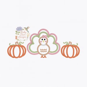May include: An embroidered design featuring a turkey with a pink bow, a pearl necklace, and a pumpkin on each side. The turkey has a light brown body and a pink and green tail. The pumpkins are orange. The text "Ruby Dear Designs" is in the upper left.
