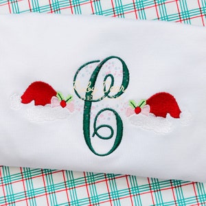 May include: A green embroidered letter "C" with two red and white Santa hats on either side. The hats have green holly leaves and red berries.