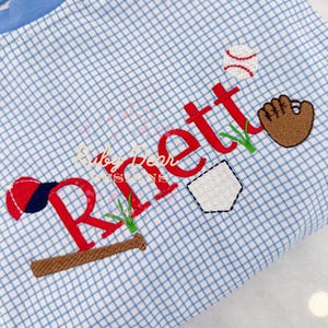 May include: A blue and white gingham fabric with red embroidered text that says "Rnett" with baseball-themed imagery including a baseball, bat, glove, and home plate.