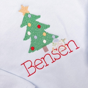 Puede incluir: Sudadera azul claro con un árbol de Navidad bordado. El árbol verde tiene adornos coloridos y una estrella dorada. El nombre "Bensen" está bordado en rojo debajo. El diseño está en la parte delantera.