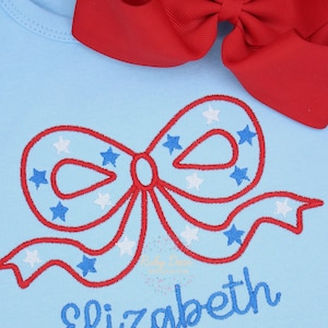 May include: A light blue baby onesie with a red, white and blue embroidered bow and the name "elizabeth" in blue embroidery.