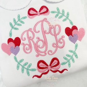 May include: A white embroidered shirt with a pink and red monogram, hearts, and bows. The monogram is "RJL" and the shirt has a scalloped collar.