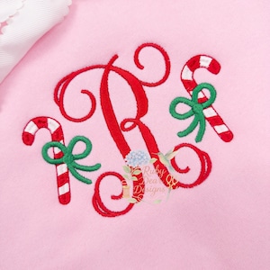 Può includere: Felpa rosa ricamata con una grande lettera "R" rossa e due bastoncini di zucchero con fiocchi verdi. I bastoncini di zucchero sono a righe rosse e bianche. Il testo "Ruby Dear Designs" è anch'esso ricamato.