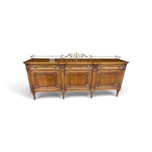May include: A long wooden sideboard featuring three central cabinet doors and three drawers above them. The piece has a polished brown wood grain finish, decorative metal hardware, and a metal gallery rail along the top edge with a central ornament.