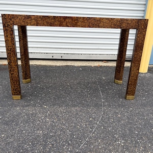 May include: A rectangular table with a brown, patterned top and legs. The legs are dark brown with a similar pattern and have brass-colored accents at the base. The table is approximately 30 inches long.