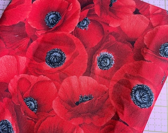 Puede incluir: Un trozo de tela roja doblada, cubierto densamente con grandes flores de amapolas rojas. Cada flor tiene un centro azul-negro oscuro. La tela es probablemente de algodón o un material similar, adecuado para proyectos de costura.