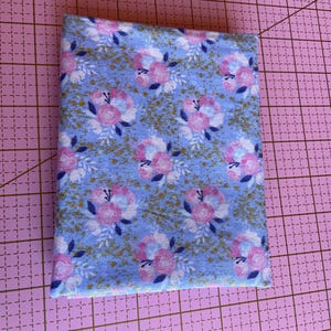 May include: A blue fabric with a white and pink floral pattern and gold glitter. The fabric is folded in half and is on a pink cutting mat.