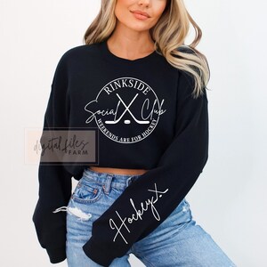 May include: Black cropped sweatshirt with a white circle graphic that says "rinkside social club" with hockey sticks and the text "weekends are for hockey". The sweatshirt has a white "hockey" written on the sleeve.