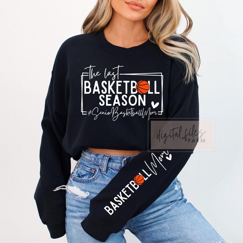 May include: Black sweatshirt with white text that reads "The last basketball season #SeniorBasketballMom" with a basketball graphic and a heart. The sweatshirt has a long sleeve with the text "Basketball Mom" and a heart.