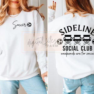 May include: White sweatshirt with black text and a soccer ball graphic on the front. The back of the sweatshirt has black text that reads "Sideline Social Club" with three director's chairs and soccer balls. The text below the chairs reads "Weekends are for soccer."