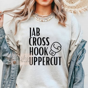 May include: A grey sweatshirt with black text that reads "Jab Cross Hook Uppercut" and a black boxing glove graphic.