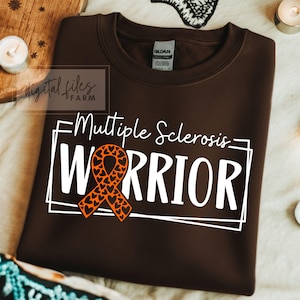 Może przedstawiać: Brązowa bluza z napisem "Multiple Sclerosis WARRIOR" w kolorze białym oraz pomarańczową wstążką z wycięciami w kształcie serca. Bluza ma okrągły dekolt i długie rękawy. Obraz zawiera również tekst "digital files FARM".