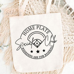 May include: White canvas tote bag with a black and white graphic design. The graphic features a baseball diamond, a baseball, and the text "Home Plate Social Club Weekends Are For Baseball".