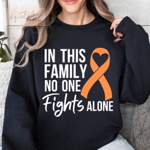 Puede incluir: Sudadera negra con el texto "In this family no one fights alone" en letras blancas. Una cinta naranja con forma de corazón está a la derecha del texto.