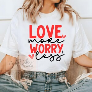 Peut inclure: T-shirt blanc avec le texte "LOVE more WORRY less" en lettres rouges et noires avec de petits cœurs.