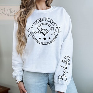 May include: White sweatshirt with a black graphic that says "Home Plate Social Club Weekends Are For Baseball" with a baseball and bat graphic. The right sleeve has a black graphic that says "Baseball" with a baseball graphic.