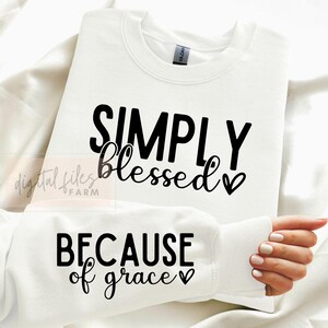 Könnte beinhalten: Weißer Pullover mit dem Text "SIMPLY blessed" und einem Herzsymbol oben und "BECAUSE of grace" und einem Herzsymbol unten.