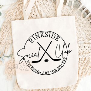May include: White canvas tote bag with a black circle logo that says "Rinkside Social Club" with two crossed hockey sticks and a puck. The text below the logo says "Weekends are for hockey."