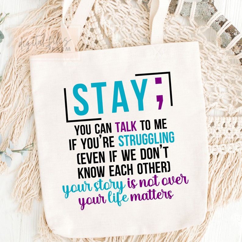 K&ouml;nnte beinhalten: Eine wei&szlig;e Einkaufstasche mit dem Text "STAY; YOU CAN TALK TO ME IF YOU'RE STRUGGLING (EVEN IF WE DON'T KNOW EACH OTHER) your story is not over your life matters" in Schwarz, Blau und Lila gedruckt.