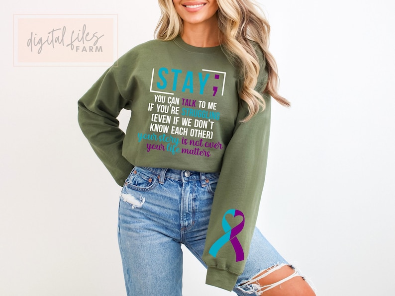 K&ouml;nnte beinhalten: Gr&uuml;ner Pullover mit dem Text "STAY; YOU CAN TALK TO ME IF YOU'RE STRUGGLING (EVEN IF WE DON'T KNOW EACH OTHER) YOUR STORY IS NOT OVER YOUR LIFE MATTERS" in T&uuml;rkis und Lila. Der Pullover hat ein t&uuml;rkisfarbenes und lilafarbenes Band am &Auml;rmel.