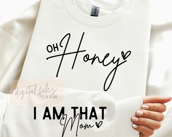 Puede incluir: Sudadera blanca con texto negro que dice "Oh Honey" en la parte superior y "I Am That Mom" en la parte inferior. Ambas frases tienen un pequeño símbolo de corazón.