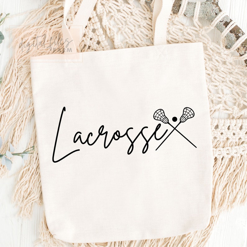 Może przedstawiać: Biała torba z pł&oacute;tna z czarnym tekstem, kt&oacute;ry m&oacute;wi "Lacrosse" i parą kij&oacute;w do lacrosse z piłką w środku.