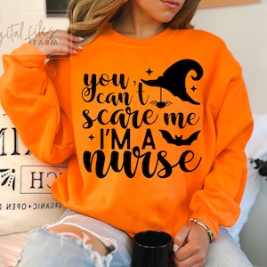 May include: Orange sweatshirt with a black graphic that says "You can't scare me I'm a nurse" with a witch's hat, spider, and bat.