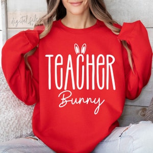 以下が含まれることがあります： 「Teacher Bunny」と白文字で書かれた赤いスウェットシャツ。Teacherの上にはウサギの耳が描かれている。