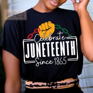 May include: Black t-shirt with a white graphic that says "Celebrate Juneteenth Since 1865". The graphic features a raised fist breaking free from chains in the colours of the Pan-African flag.