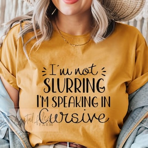 May include: A mustard yellow t-shirt with black text that reads "I'm not slurring I'm speaking in cursive".