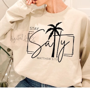 May include: A beige sweatshirt with the words "Stay Salty" in a black script font, with a black palm tree graphic. The text "Matthew 5:13" is below the word "Salty".