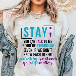 K&ouml;nnte beinhalten: Ein wei&szlig;es T-Shirt mit einer blaugr&uuml;nen und violetten Grafik, auf der "STAY; YOU CAN TALK TO ME IF YOU'RE STRUGGLING (EVEN IF WE DON'T KNOW EACH OTHER) your story is not over your life matters" steht.