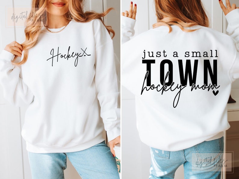 Może przedstawiać: Biała bluza z czarnym napisem z przodu, kt&oacute;ry brzmi "Hockey" i czarnym napisem z tyłu, kt&oacute;ry brzmi "Just a small town hockey mom" z małym sercem.