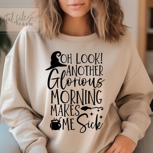 Peut inclure: Un sweat-shirt beige avec un imprimé graphique noir qui dit "Oh look! Another glorious morning makes me sick". Le graphique comprend un chapeau de sorcière, un chaudron et un balai.