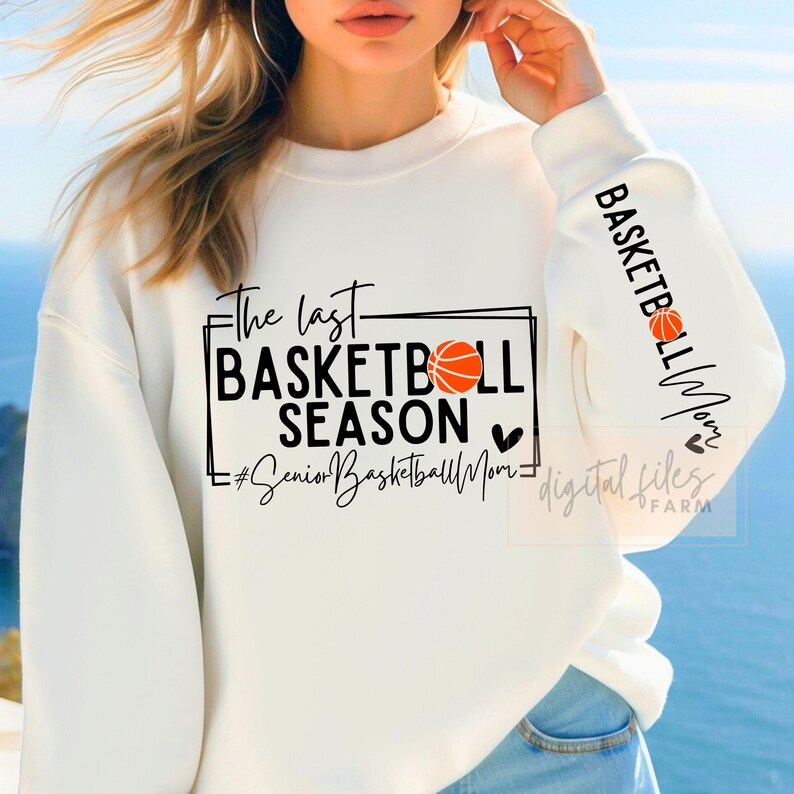 May include: White sweatshirt with black text that reads "The last basketball season #SeniorBasketballMom" with a basketball graphic and a heart. The sleeve has black text that reads "Basketball Mom" with a heart.
