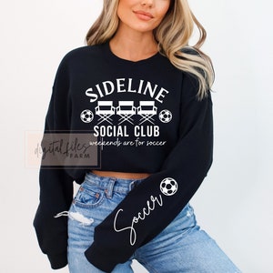 May include: Black cropped sweatshirt with white text that reads "Sideline Social Club" and "Weekends are for soccer". The sweatshirt has a soccer ball graphic on the sleeve and the word "Soccer" written in cursive.