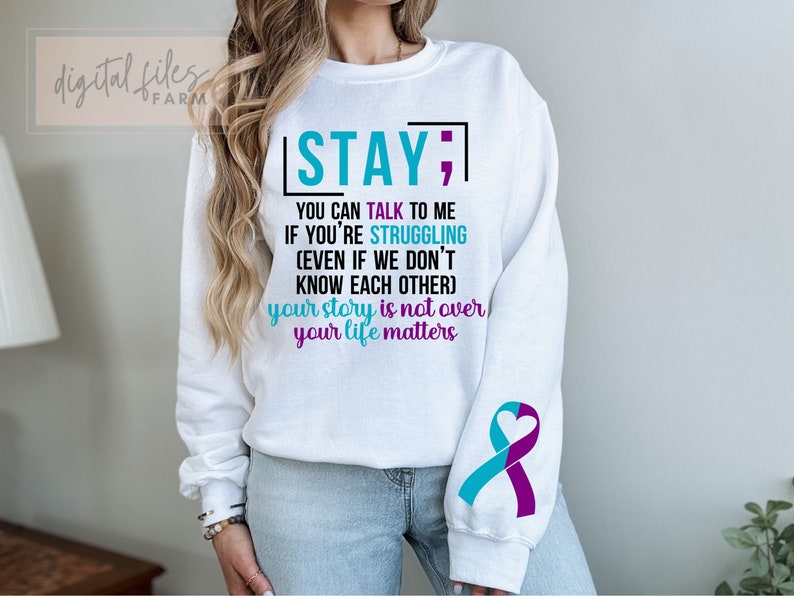 K&ouml;nnte beinhalten: Wei&szlig;er Pullover mit einem t&uuml;rkisfarbenen und violetten Band am &Auml;rmel. Der Text auf dem Pullover lautet "STAY; YOU CAN TALK TO ME IF YOU'RE STRUGGLING (EVEN IF WE DON'T KNOW EACH OTHER) your story is not over your life matters".